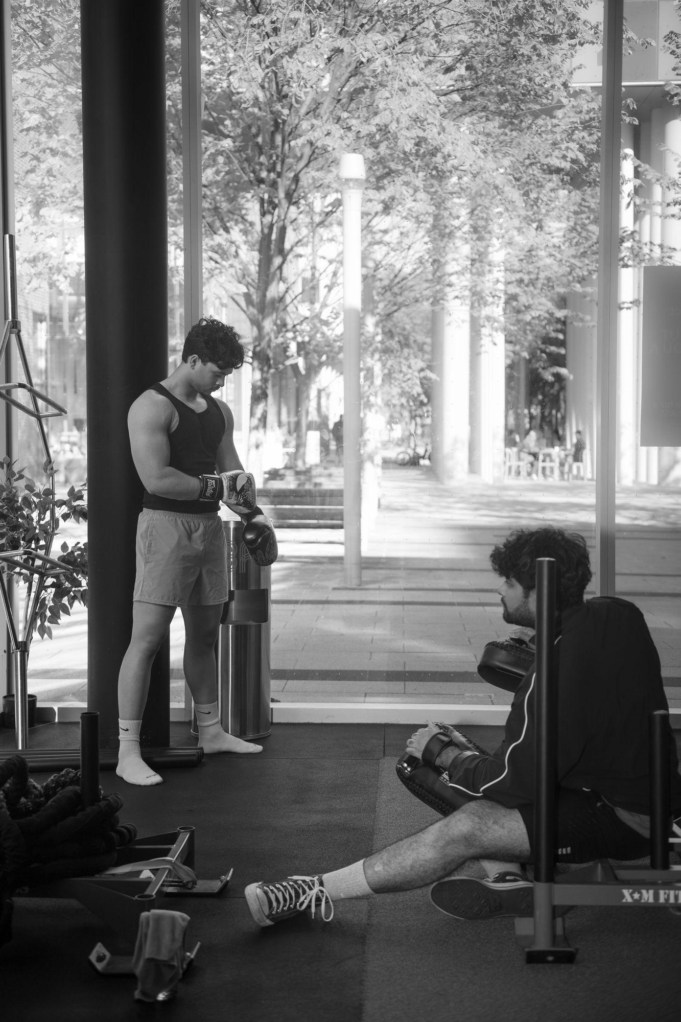 Boxer wrapping his gloves while his coach waits with pads by the studio window